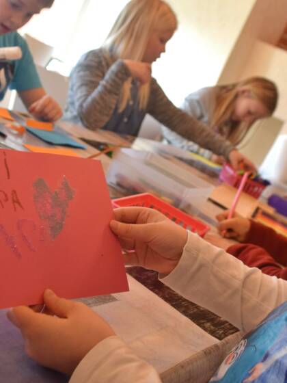 En grupp barn som pysslar. Ett barn visar en teckning.